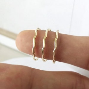 Może przedstawiać: Cztery złote faliste pierścienie ułożone na palcu.