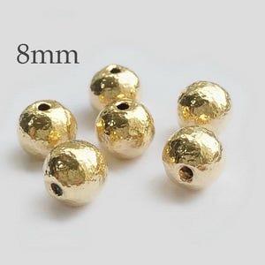 May include: Six gold-coloured, 8mm round beads with a hammered texture. The beads have a hole in the centre for stringing.