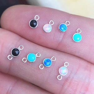 Op de afbeelding: Assortiment van kleine, ronde edelsteenbedels met zilveren springringen. De bedels zijn in zwart, wit, blauw en turquoise.