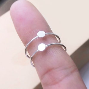 May include: Two silver rings with a small round disc on each. The rings are stacked on top of each other.