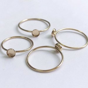 Op de afbeelding: Vier gouden ringen met ronde bezels. De bezels zijn leeg en klaar om te worden gevuld met stenen of andere versieringen.