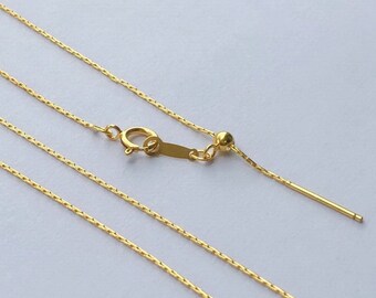 May include: Three gold chains with a clasp and a small ball at the end of the chain. The chains are laid out in parallel lines on a white surface.
