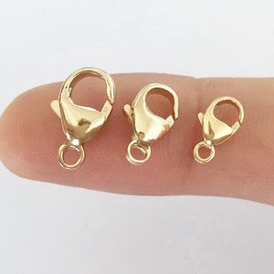 May include: Three gold-toned lobster clasps of different sizes. The clasps are shown on a finger.