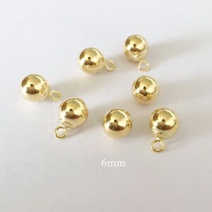 May include: Six gold-colored metal ball charms with a loop for attaching to jewelry or other crafts. Each ball is 6mm in diameter.