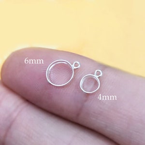 Könnte beinhalten: Zwei silberne Sprungringe mit einer runden Öffnung. Der größere Ring misst 6 mm und der kleinere Ring misst 4 mm.