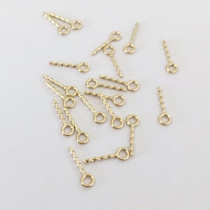 May include: A group of gold-coloured twisted head pins with small loops at the top. These pins are commonly used in jewellery making and crafting.