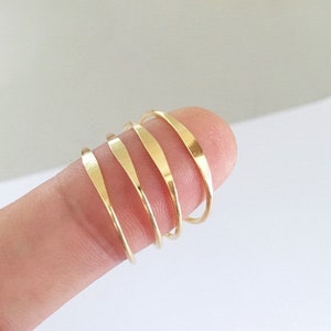 Puede incluir: Un conjunto de cinco anillos apilables de color dorado. Los anillos son finos y tienen una textura ligeramente martillada.