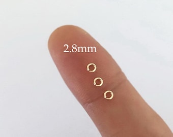 May include: Four gold jump rings, each measuring 2.8 mm in diameter, are displayed on a finger.