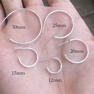 May include: A selection of silver hoop earrings in different sizes: 30mm, 25mm, 20mm, 15mm, and 12mm. The earrings are shown on a hand, displaying their varying diameters. The image emphasizes the range of sizes available.