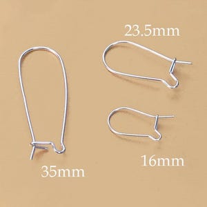 May include: Three silver earring hooks of different sizes are shown on a tan backdrop. The largest hook measures 3.5cm, the medium hook is 2.35cm, and the smallest is 1.6cm. These are likely for jewellery making.