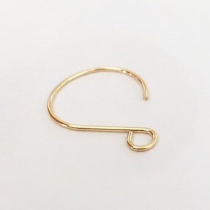 May include: A single gold-colored earring hook, set against a white background. The hook is a simple, curved design with a loop at the bottom. The metal has a shiny finish.