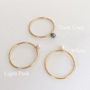 Könnte beinhalten: Drei goldene Ringe mit jeweils einer kleinen Perle. Die Perlen sind hellrosa, weiß und dunkelgrau.