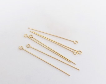 Può includere: Un gruppo di sei spilli per la testa dorati con anelli. Gli spilli per la testa sono disposti in modo casuale su una superficie bianca.