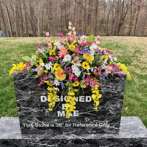 May include: A black and gray marble-like stone with the words "DESIGNED BY ME" and a floral arrangement. The flowers are a mix of yellow, pink, purple, and white. The stone is 36 inches for reference.