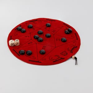 May include: A red felt game board with black playing pieces and two white dice. The board is divided into sections with numbers and symbols.
