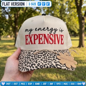 May include: A cream-colored baseball cap with a leopard print brim. The front features black cursive text reading my energy is and red block text reading EXPENSIVE. A flower-shaped cardboard tag labeled MINOSHStudio is attached to the brim.