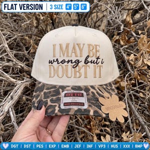 May include: A cream-coloured baseball cap with a leopard print brim. The front features embroidered text that reads I MAY BE wrong but i DOUBT IT. The cap includes a sticker on the brim and a flower-shaped tag labelled MINOSHStudio.