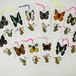 May include: A set of 12 oval-shaped bookmarks featuring different butterfly specimens. Each bookmark has a white background with a butterfly mounted in the centre and a floral design around it.