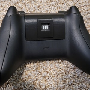 May include: Black wireless gaming controller with a textured surface and a small rectangular button with three white lines on the back.