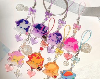 May include: A collection of colorful acrylic charms featuring cartoon pony characters. Each charm has a different color scheme and is adorned with heart-shaped pendants, bows, and beads. The charms are attached to purple lanyards.