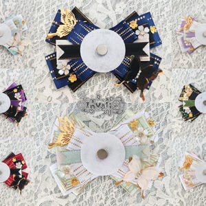 May include: Assortment of decorative bow hair accessories in various colors, including blue, purple, and pink. Each bow features a central white disc, decorative butterflies, and floral accents. The bows are arranged on a white lace surface.