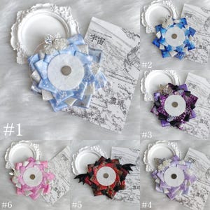 May include: A collection of handmade decorative hair accessories. Each features a central white circle surrounded by layered ribbon in various colors, including blue, purple, pink, and red. Some have floral or bat wing accents. The Japanese text "宇宙" is visible.