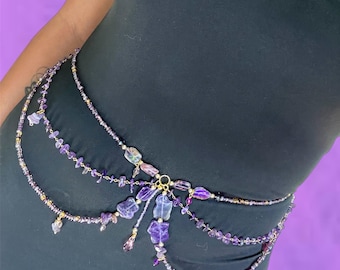 May include: A multi-layered waist chain featuring purple amethyst stones and small beads. The chain has a gold-colored clasp and accents. The amethyst stones vary in shape and size, adding a unique touch to the accessory.
