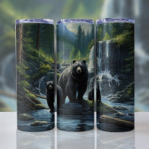 May include: A stainless steel tumbler with a black bear and two cubs standing in a forest stream with a waterfall in the background. The tumbler has a black and green design.