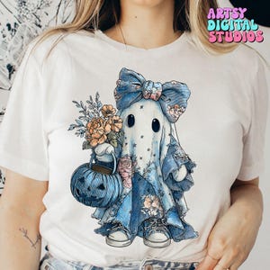 Puede incluir: Camiseta blanca con un personaje de fantasma caprichoso con un lazo azul, detalles florales y una cesta con forma de calabaza. El fantasma lleva zapatillas y sostiene un ramo. El texto "ARTSY DIGITAL STUDIOS" se muestra en la esquina superior derecha.
