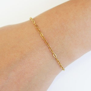 May include: A gold chain bracelet on a person's wrist.