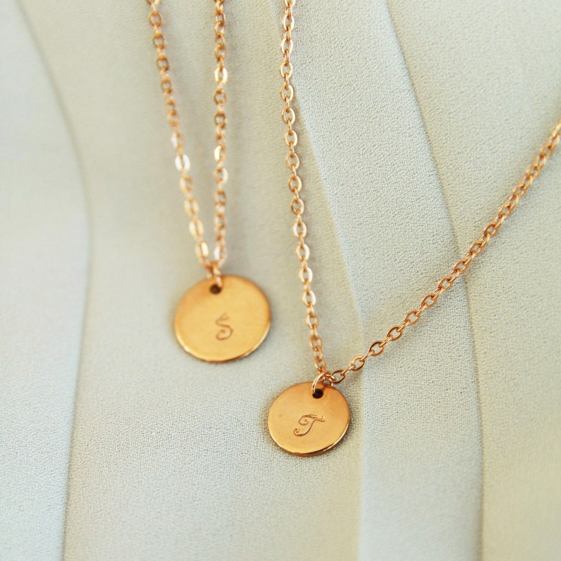 Puede incluir: Dos collares de oro con colgantes redondos. Los colgantes est&aacute;n grabados con las letras "S" y "T".