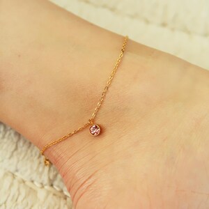 May include: A delicate gold anklet with a small pink crystal charm.