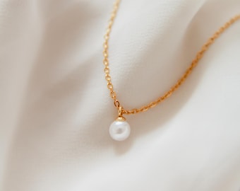 May include: A delicate gold chain necklace with a single white pearl pendant.