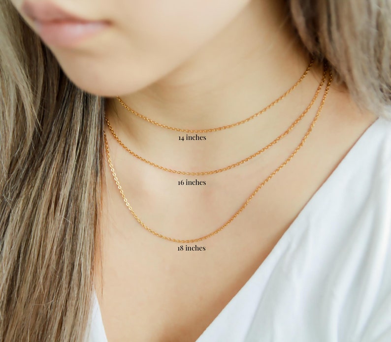 Puede incluir: Tres cadenas de oro de diferentes longitudes, 14 pulgadas, 16 pulgadas y 18 pulgadas, se muestran en el cuello de una modelo.
