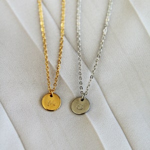 Puede incluir: Dos delicados collares con colgantes redondos, uno dorado con la letra "M" y otro plateado con la letra "E".