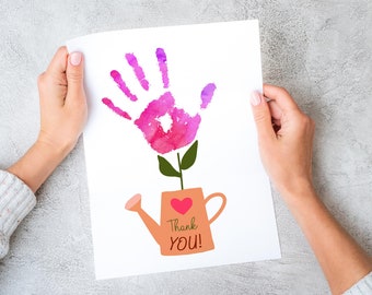 May include: A white card with a pink handprint flower growing out of a pink watering can. The watering can has a red heart and the text "Thank You!" on it.