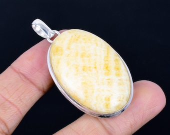 以下が含まれることがあります： 銀色の金属フレームにセットされた、淡い黄色の石を使用した楕円形のペンダント。石は質感があり、ペンダントの上部にはチェーン用の小さなループが付いています。背景は黒です。