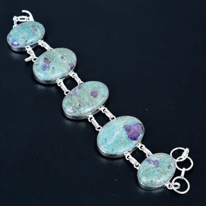 May include: A silver link bracelet featuring five oval-shaped cabochons of green fuchsite stone with embedded magenta-coloured ruby inclusions. The stones are set in polished silver bezels and connected by small silver rings with a clasp at the end.