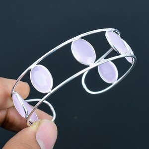 Könnte beinhalten: Ein silbernes Armreif-Armband mit fünf ovalen, hellvioletten Edelsteinen, die in den Metallrahmen gefasst sind.