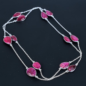 Puede incluir: Un collar de cadena de plata con múltiples piedras preciosas en forma de lágrima de rubí. El collar está en capas y tiene una cadena delicada.