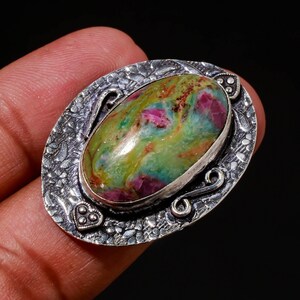 Könnte beinhalten: Ein silberner Ring mit einem ovalen, grün-rosa Edelstein, der in eine detailreiche Silberfassung gefasst ist.
