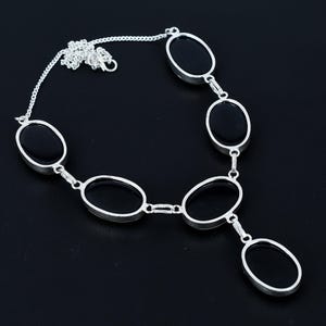 Puede incluir: Un collar plateado con piedras negras de forma ovalada. El collar tiene una cadena fina y est&aacute; compuesto por varias piedras ovaladas conectadas, creando un dise&ntilde;o elegante. Las piedras est&aacute;n engastadas en un marco de metal plateado.
