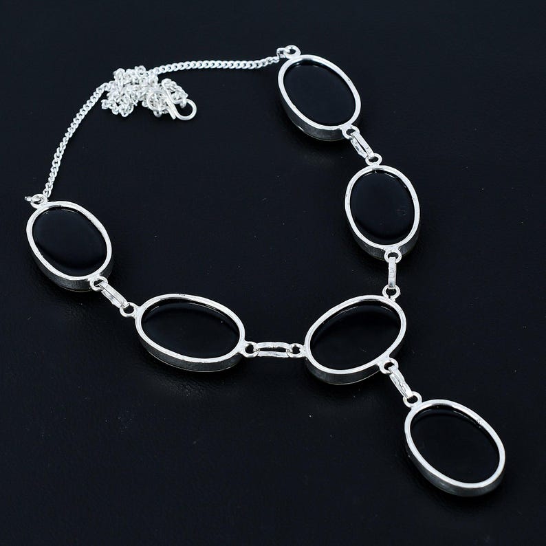 Puede incluir: Un collar plateado con piedras negras de forma ovalada. El collar tiene una cadena fina y est&aacute; compuesto por varias piedras ovaladas conectadas, creando un dise&ntilde;o elegante. Las piedras est&aacute;n engastadas en un marco de metal plateado.