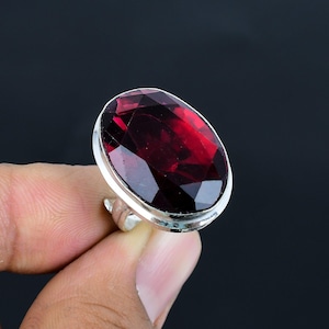May include: A silver ring with a large, oval-shaped, faceted, dark red gemstone.