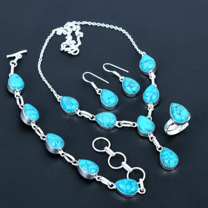 Könnte beinhalten: Ein komplettes Schmuckset mit Halskette, Armband, Ohrringen und Ring. Jedes Stück hat eine silberne Fassung und ist mit tropfenförmigen türkisfarbenen Steinen verziert. Das Set wird auf einer dunklen Oberfläche präsentiert, die die leuchtende blaue Farbe der Steine hervorhebt.