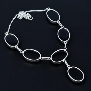 Puede incluir: Un collar plateado con piedras negras de forma ovalada. El collar tiene una cadena fina y est&aacute; compuesto por varias piedras ovaladas conectadas, creando un dise&ntilde;o elegante. Las piedras est&aacute;n engastadas en un marco de metal plateado.