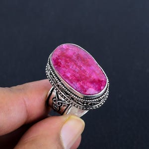 Peut inclure: Une bague en argent avec une pierre précieuse rose ovale sertie dans une bélière en argent décorative. La bague a un design complexe sur la bande.
