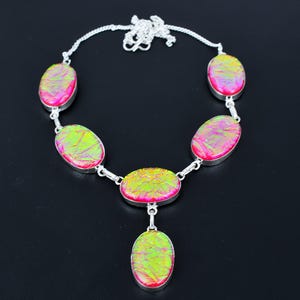 Puede incluir: Un collar de plata con piedras ovaladas e iridiscentes en tonos rosa y verde. Las piedras est&aacute;n engarzadas en plata y unidas por una cadena de plata. El collar tiene un colgante con una sola piedra ovalada.