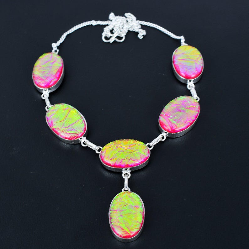 Puede incluir: Un collar de plata con piedras ovaladas e iridiscentes en tonos rosa y verde. Las piedras est&aacute;n engarzadas en plata y unidas por una cadena de plata. El collar tiene un colgante con una sola piedra ovalada.