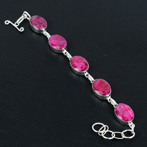 Könnte beinhalten: Ein silbernes Armband mit fünf ovalen rosafarbenen Edelsteinen. Das Armband hat einen Karabinerverschluss.